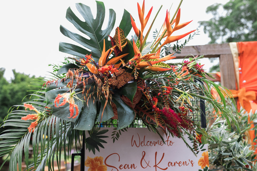 Tropical looking flowers artfully arranged in an Oshun Pouch displayed on a screen displaying the hand painted wedding schedule for a wedding 