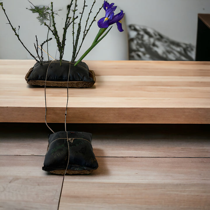 Biodegradable black brick tray used as a base for a small floral arrangement displayed on a wooden surface.