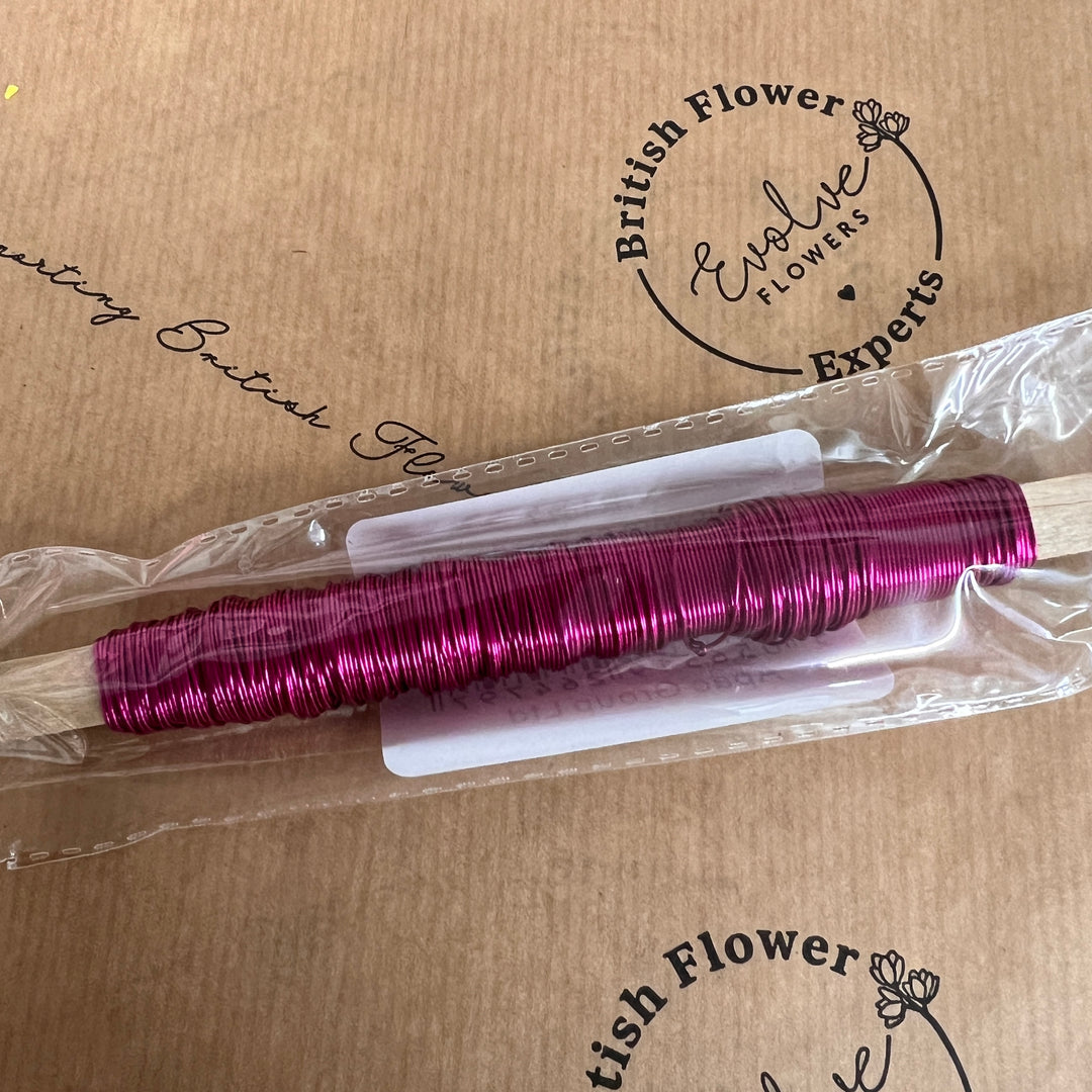 A spool of pink metallic finish steel wire on a wooden stick, packaged and labeled.