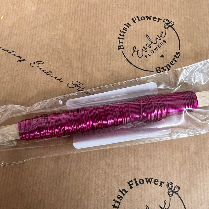 A spool of pink metallic finish steel wire on a wooden stick, packaged and labeled.