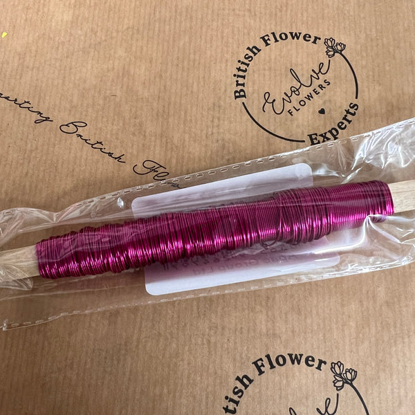 A spool of pink metallic finish steel wire on a wooden stick, packaged and labeled.