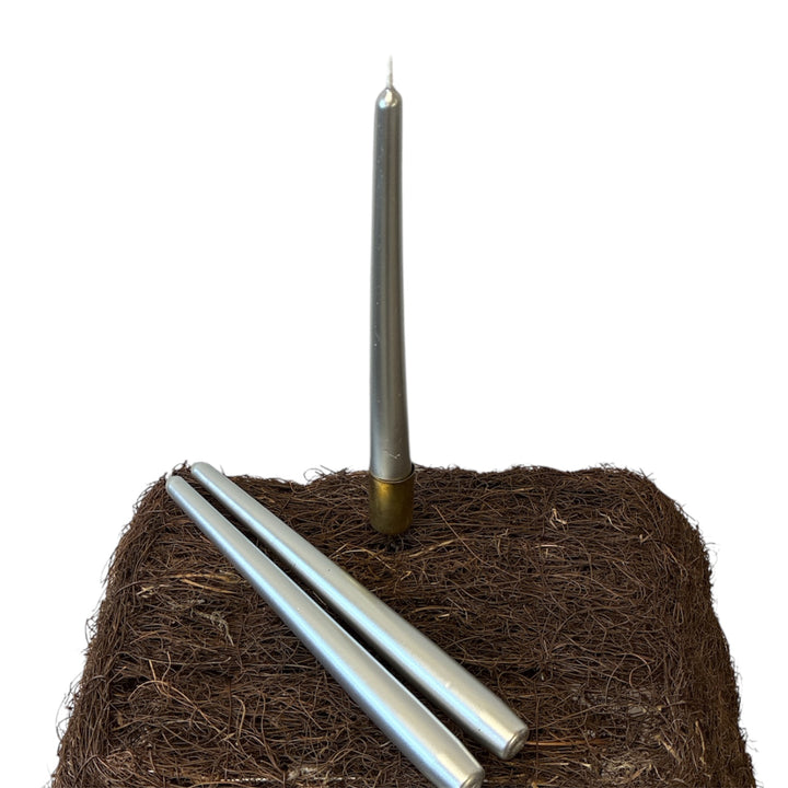 Threeo silver candles on a bed of brown vermiculite against a white background