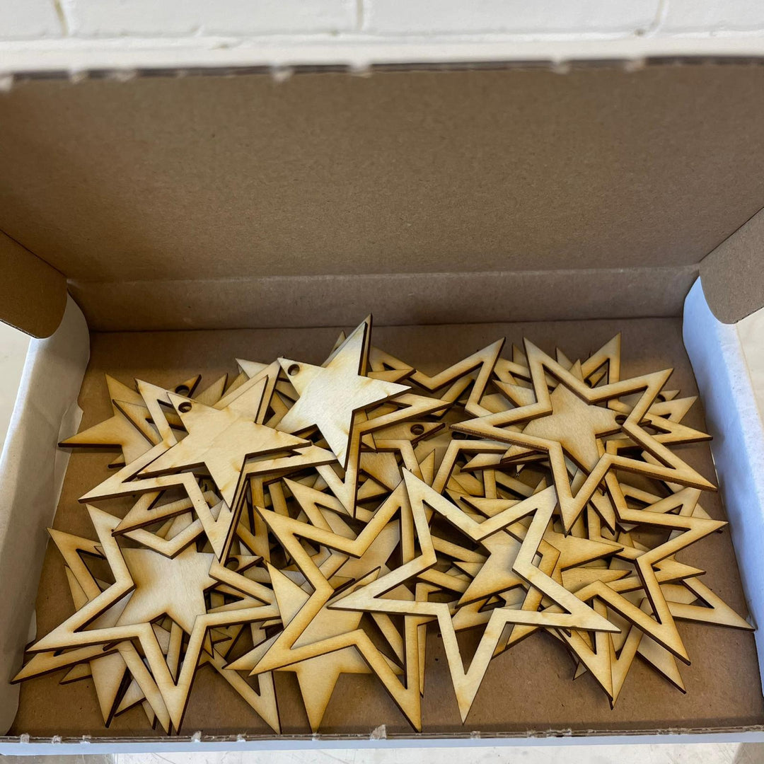 A cardboard box filled with forty laser-cut wooden stars, showing the two distinct five-point geometric designs made from light-coloured FSC timber.