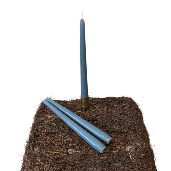Three blue candles on a bed of straw with one candle lit against a white background