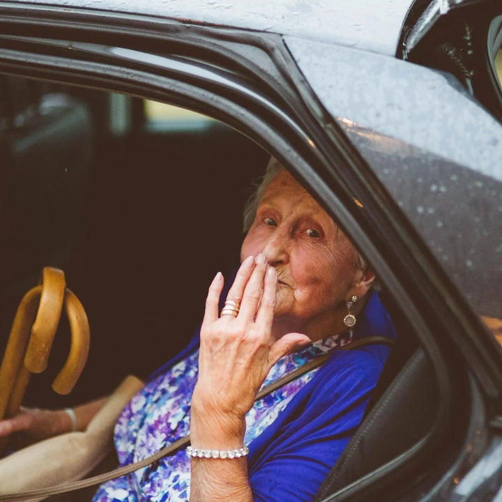 An elderly woman sitting inside a vehicle blowing a gentle kiss to the camera with a warm smile.