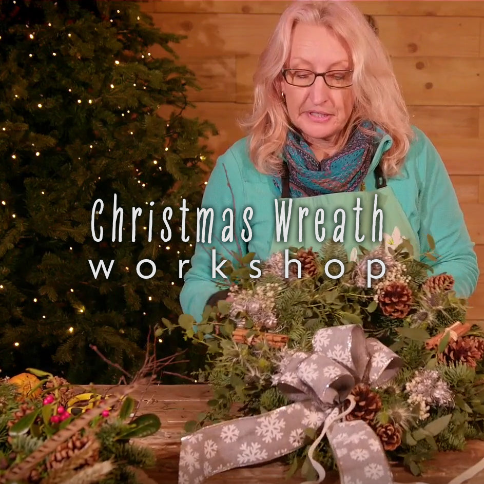 A person participating in a Christmas wreath workshop, creating a wreath with greenery and pine cones.