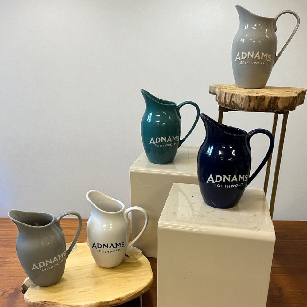 Collection of Adnams Southwold ceramic jugs on wooden and white platforms.
