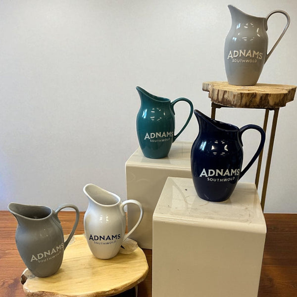 Collection of Adnams Southwold ceramic jugs on wooden and white platforms.