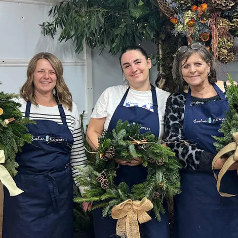 A smiling workshop participant holding a finished luxury Christmas wreath made with premium winter foliage and elegant silk ribbons at an Evolve Flowers masterclass.