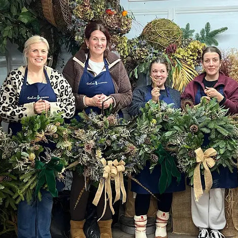 A creative entrepreneur holding her completed high-end holiday wreath inside the beautifully styled Evolve Flowers workshop space.
