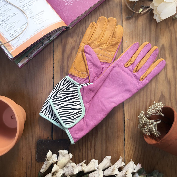 Flat lay shot of Hannah MidiGaunt zebra-cuff gloves laid on a wooden surface with garden tools, an open book, and terracotta pots.