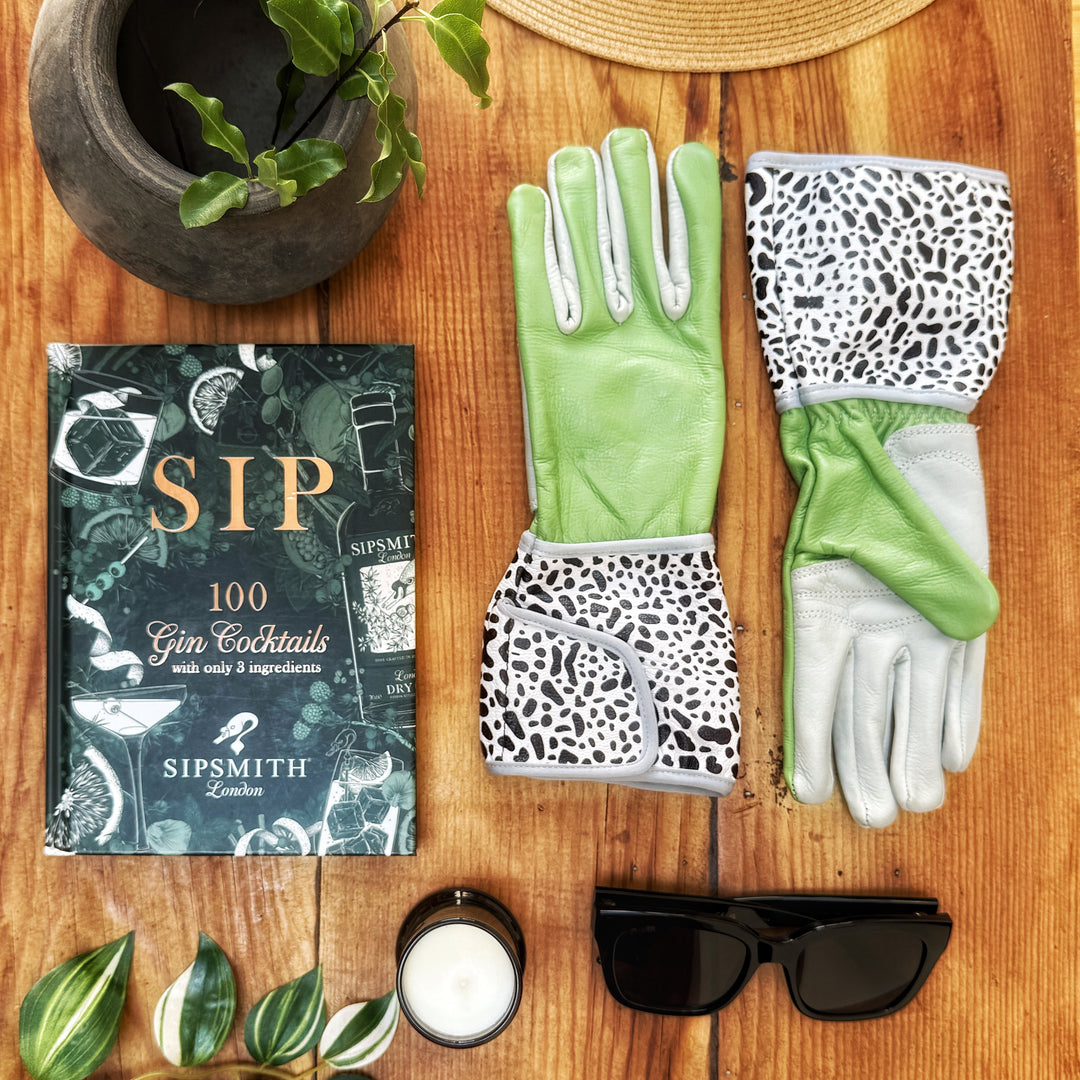 Sage, stone, and leopard-print Hilda MidiGaunt gloves displayed on a wooden surface with a sunhat, garden pot, and book.