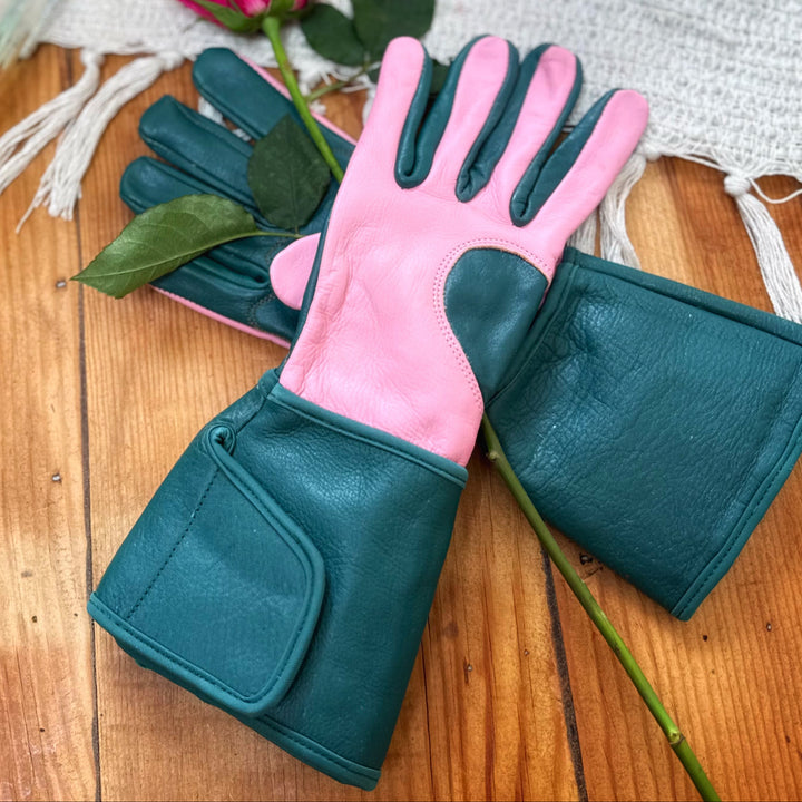 Pair of teal and candy pink Ivy MidiGaunt leather gardening gloves displayed on a wooden surface with a fresh cut pink rose.
