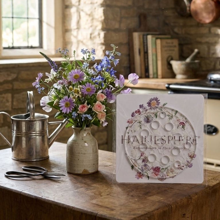 Halliesphere 10cm Eco Flower Arranger in bespoke packaging set on a rustic wooden table next to a vase of colourful British wildflowers, watering can, and florist snips