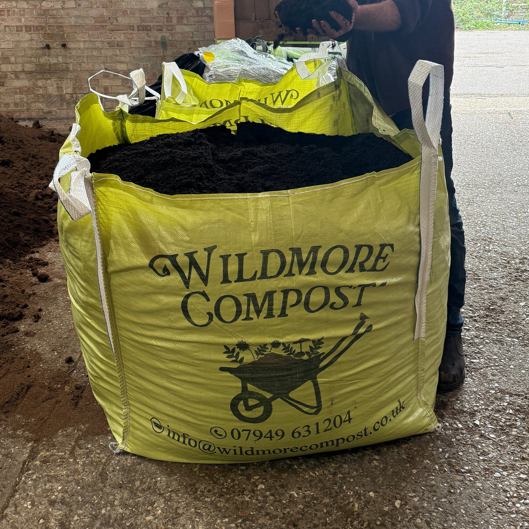 Person holding a bag of Wildmore Compost on a concrete surface with a building in the background.