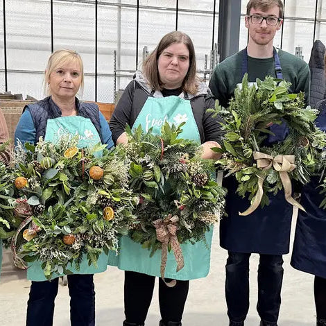 Close-up of a workshop participant holding a unique, sustainable Christmas wreath showcasing rich textures, pinecones, and natural winter accents.